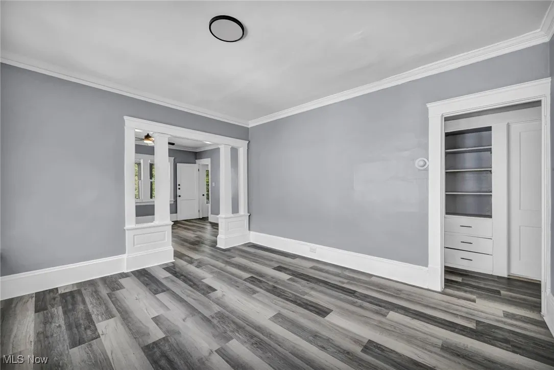 Unfurnished room featuring ornate columns, ornamental molding, and wood finished floors