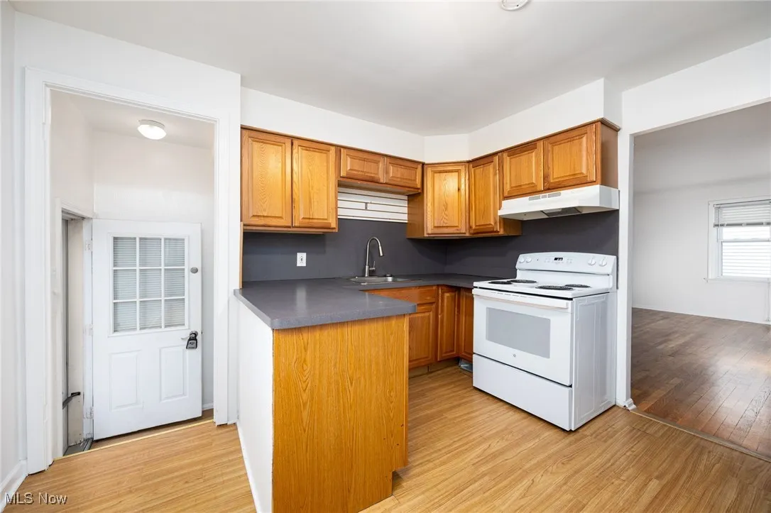 Kitchen with white range with electric stovetop, light wood-style flooring, brown cabinets, and dark countertops
