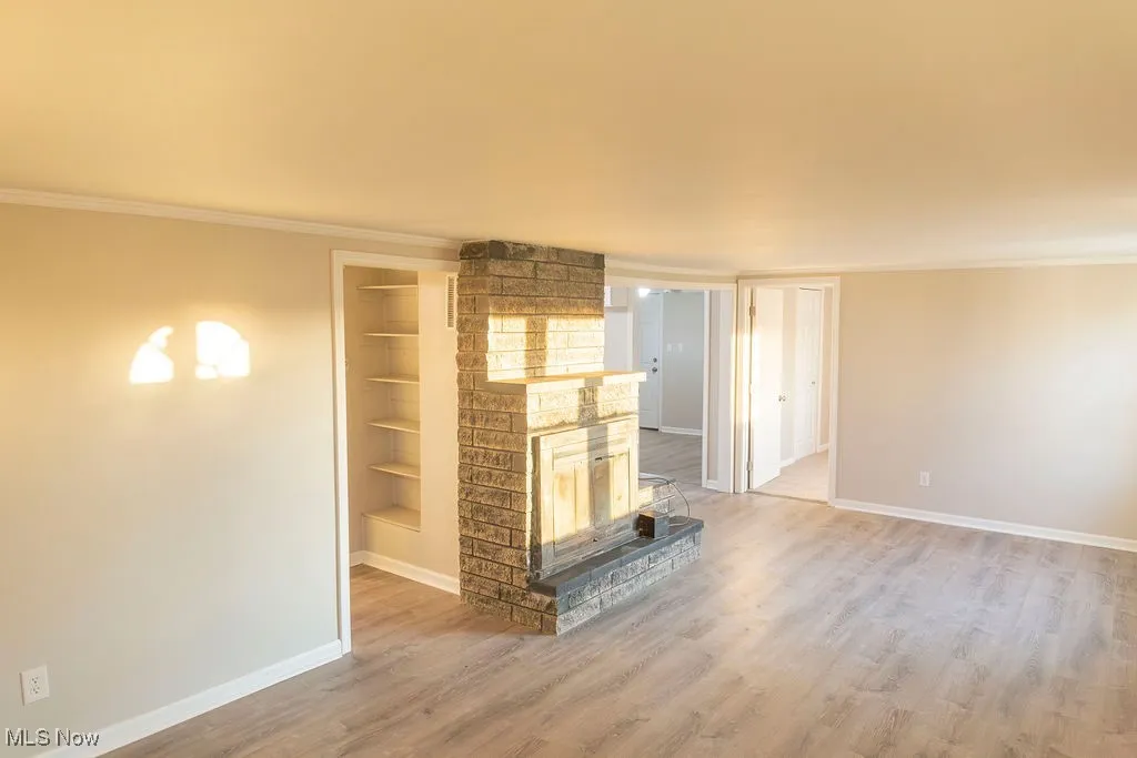 Unfurnished living room with ornamental molding, a brick fireplace, light wood-type flooring, and built in features