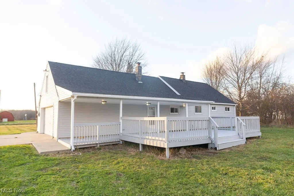 Back of property featuring a lawn, a chimney, concrete driveway, a deck, and an attached garage