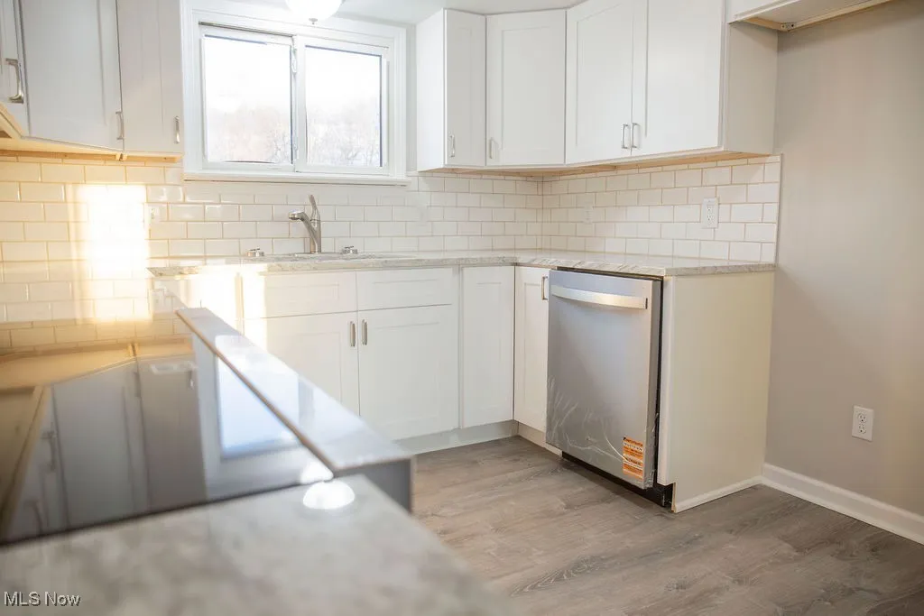 Kitchen featuring light stone countertops, white cabinets, light wood-type flooring, dishwasher, and decorative backsplash