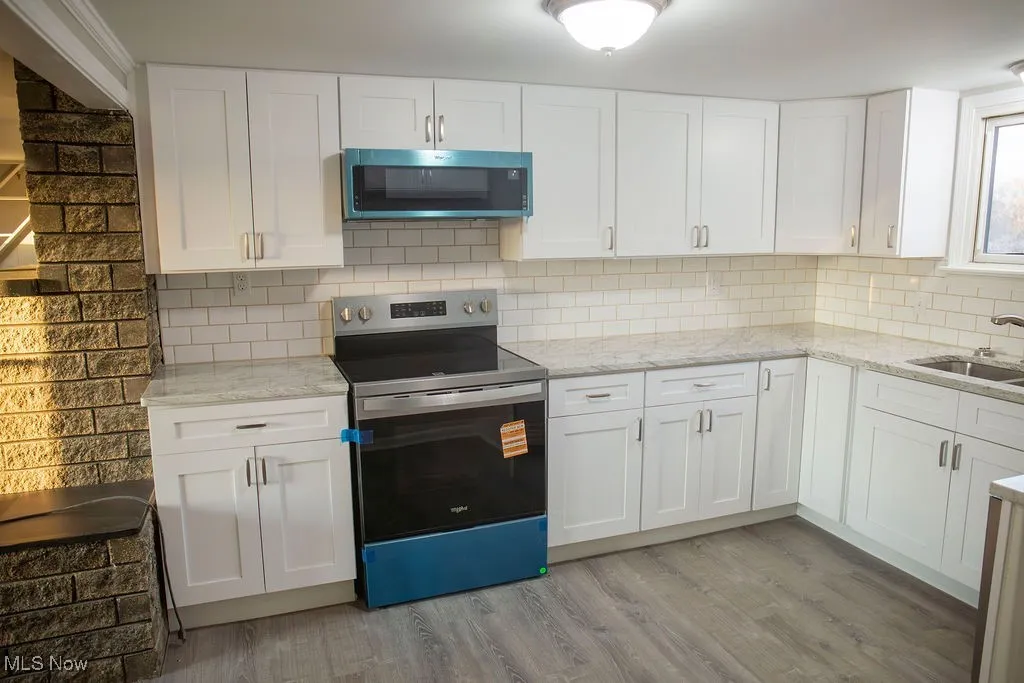 Kitchen featuring stainless steel appliances, white cabinetry, light stone counters, and light wood-style flooring
