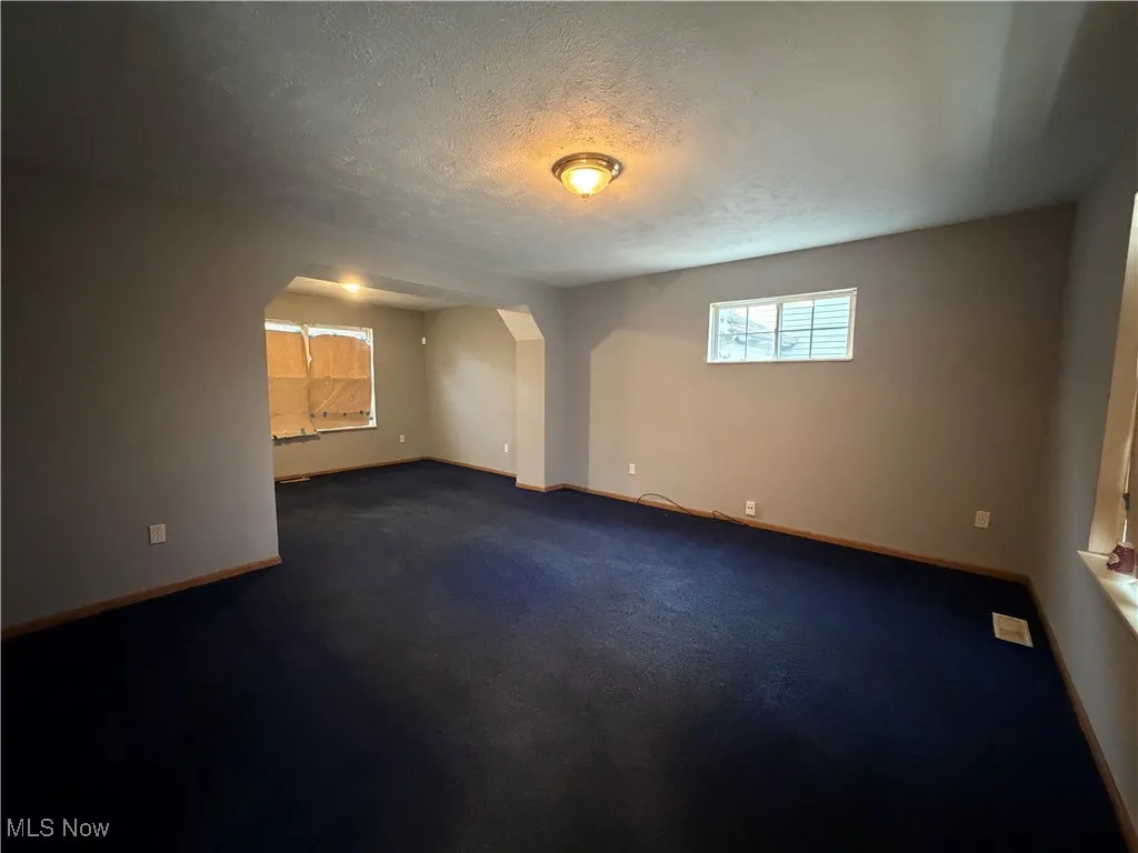 Empty room featuring arched walkways, a textured ceiling, and dark colored carpet