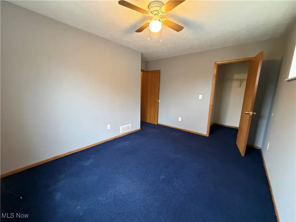 Unfurnished bedroom with a spacious closet, ceiling fan, carpet floors, and a textured ceiling
