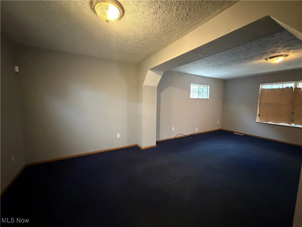 Carpeted empty room with a textured ceiling and baseboards