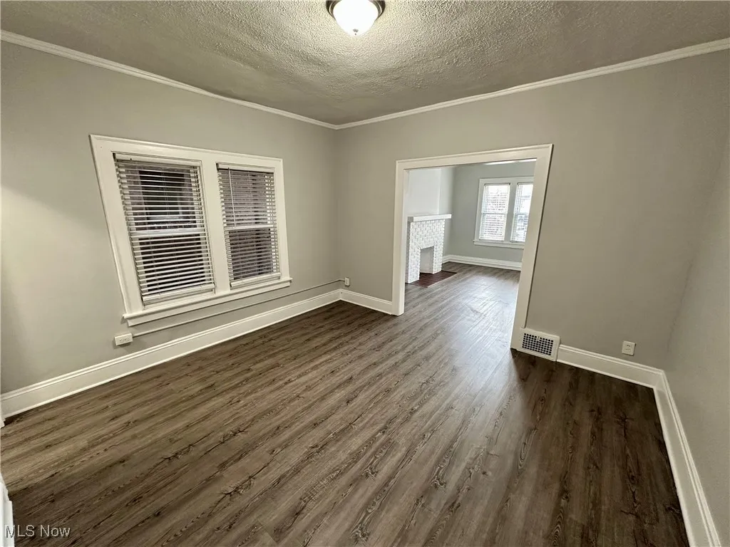 Unfurnished room with a textured ceiling, ornamental molding, and dark wood-style flooring