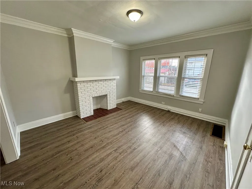 Unfurnished living room featuring a brick fireplace, dark wood-style floors, and ornamental molding