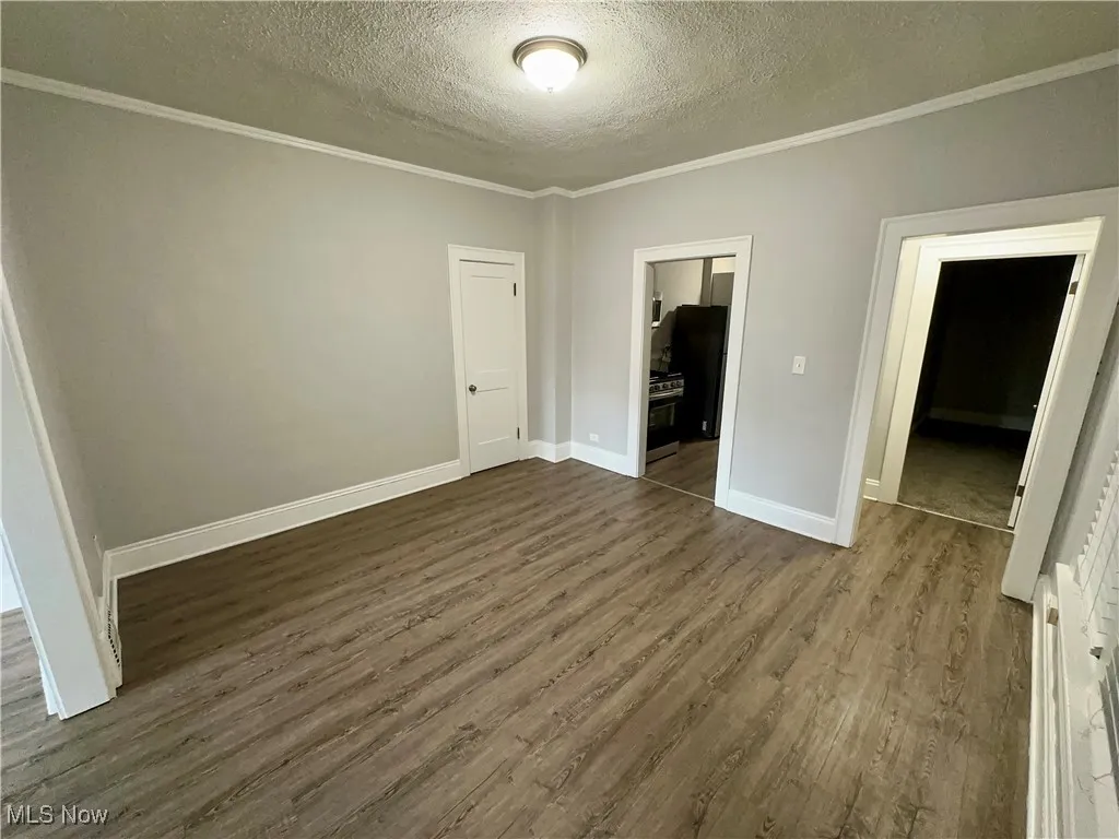 Unfurnished bedroom with a textured ceiling, ornamental molding, and dark wood-style flooring