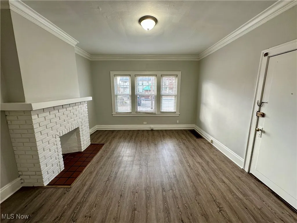 Unfurnished living room with a brick fireplace, dark wood finished floors, and ornamental molding