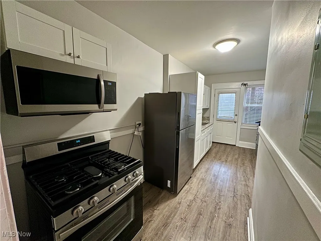 Kitchen with stainless steel appliances, white cabinets, light wood-type flooring, and light countertops