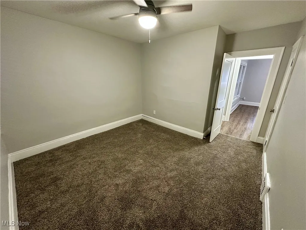 Empty room featuring dark carpet and ceiling fan