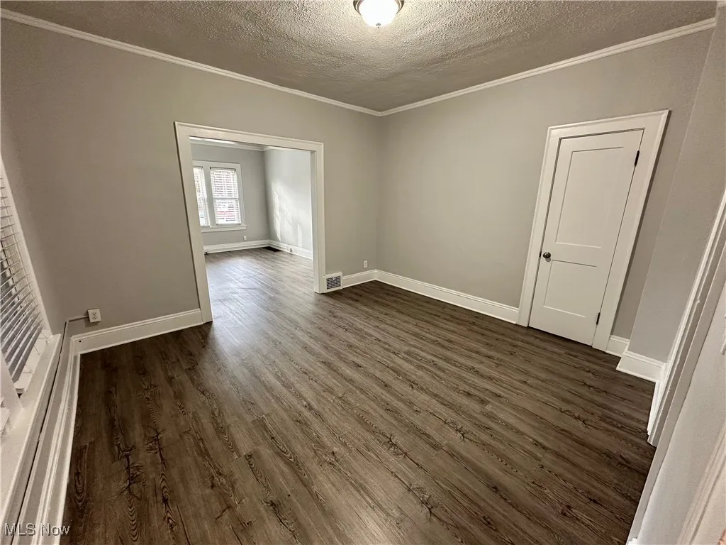 Empty room with a textured ceiling, dark wood-type flooring, and ornamental molding