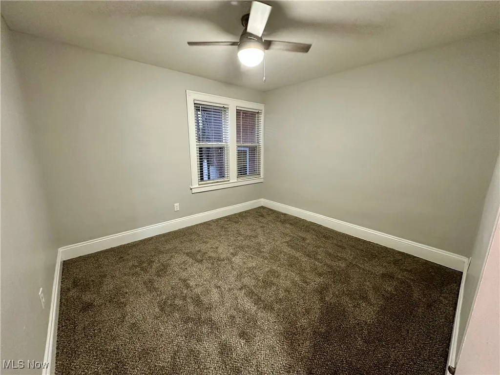 Carpeted empty room featuring baseboards and a ceiling fan