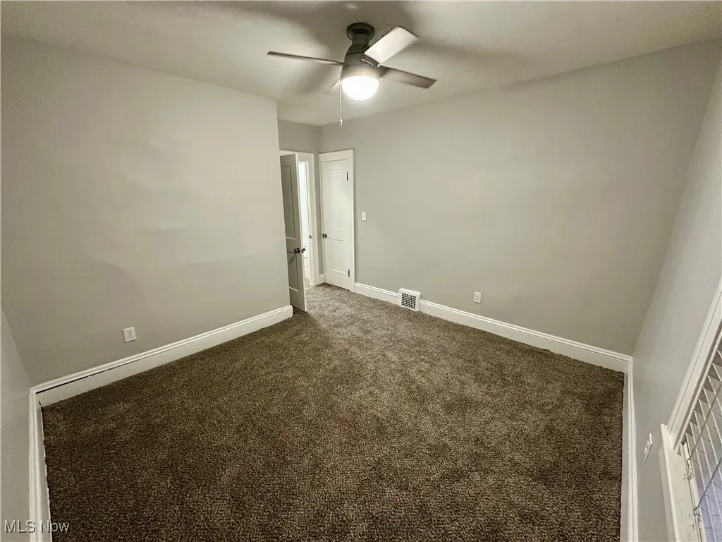 Empty room featuring dark colored carpet and ceiling fan