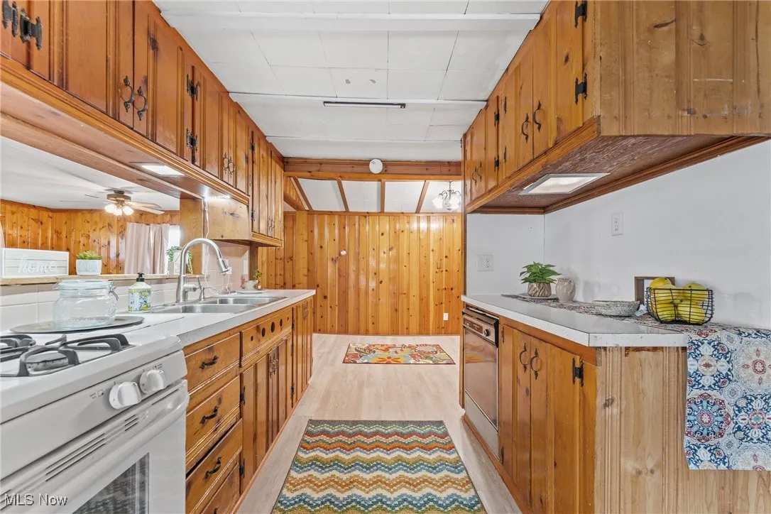 Kitchen with brown cabinetry, light countertops, wood walls, light wood-type flooring, and ceiling fan