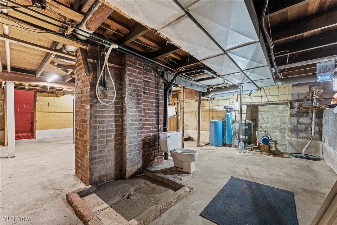 Unfinished below grade area featuring a water softener system, drainage system, and a water pressure tank