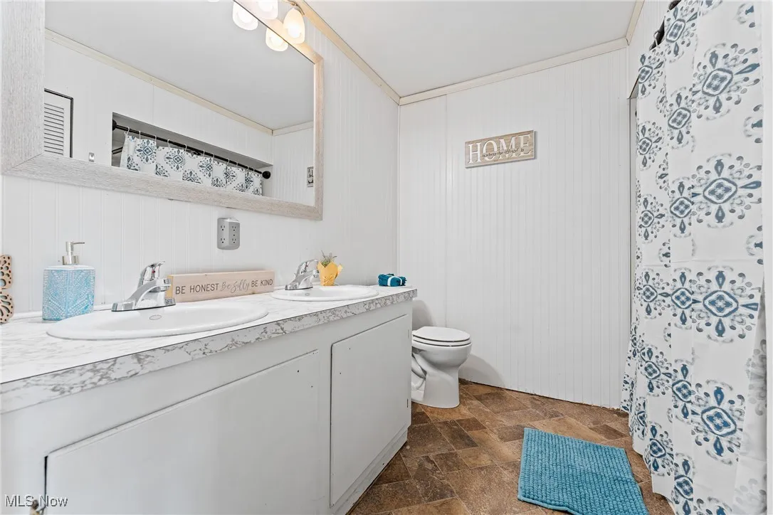 Full bathroom with curtained shower, stone finish floors, double vanity, and ornamental molding