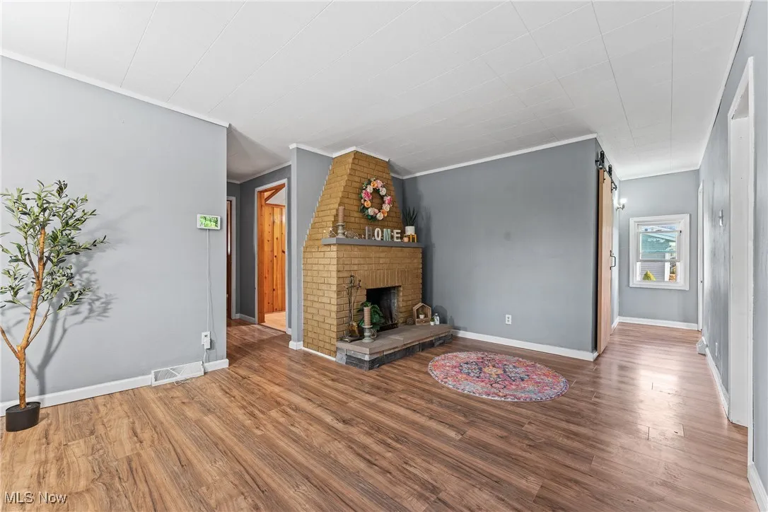 Unfurnished living room featuring wood finished floors, a brick fireplace, and ornamental molding