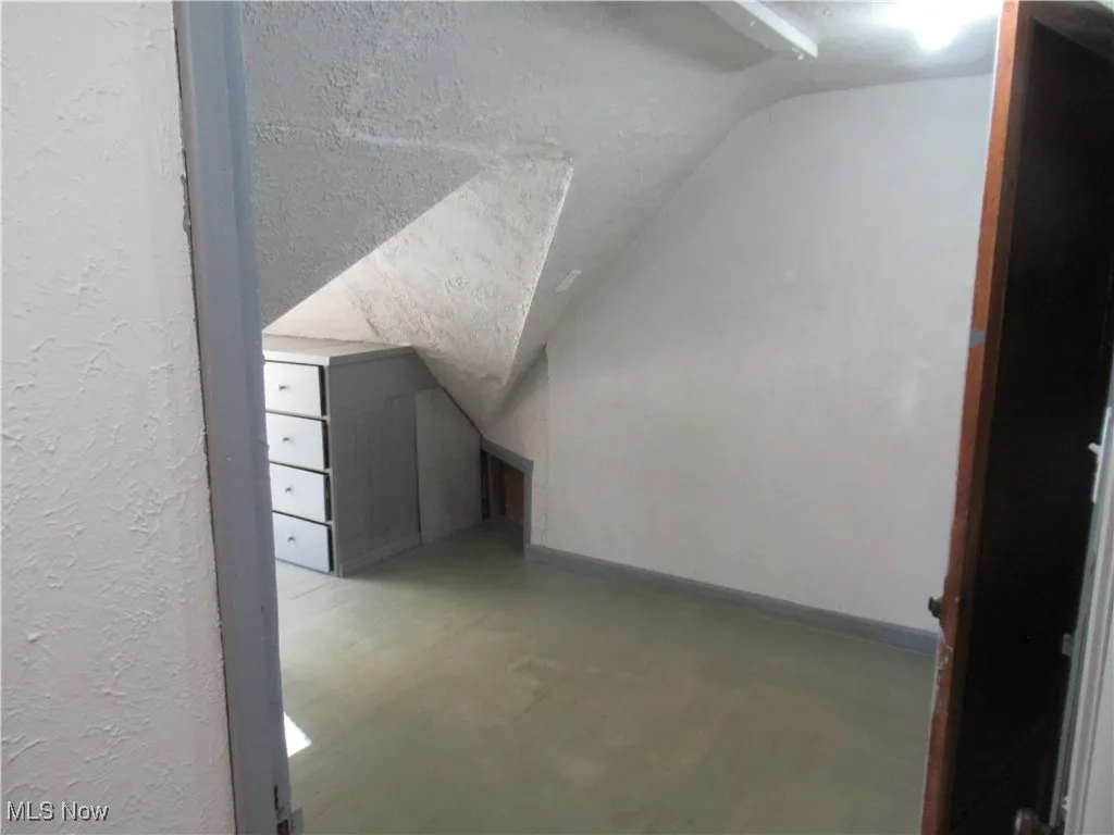 Additional living space with lofted ceiling, a textured ceiling, and a textured wall