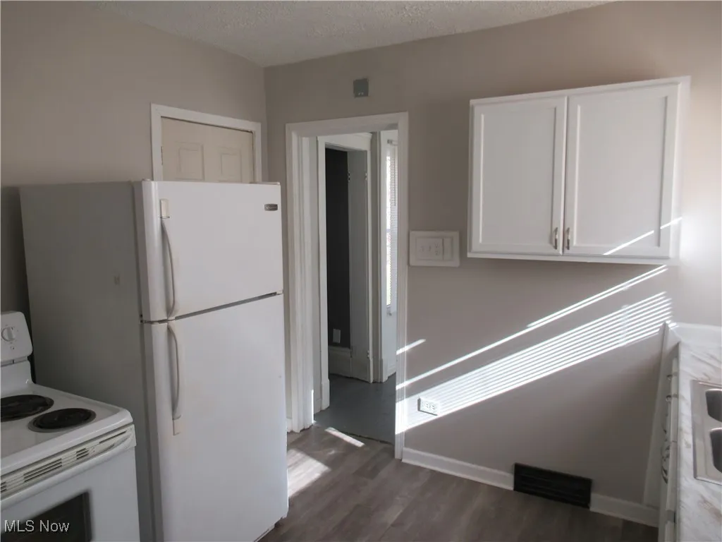 Kitchen featuring white appliances, white cabinetry, a textured ceiling, dark wood-style flooring, and light countertops
