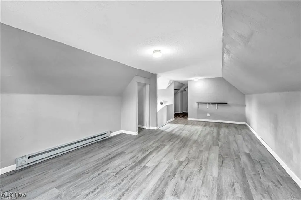 Additional living space with a textured ceiling, a baseboard heating unit, hardwood / wood-style flooring, and vaulted ceiling