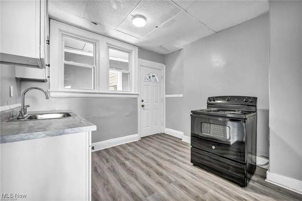 Kitchen featuring white cabinetry, a drop ceiling, light hardwood / wood-style flooring, black range with electric cooktop, and sink