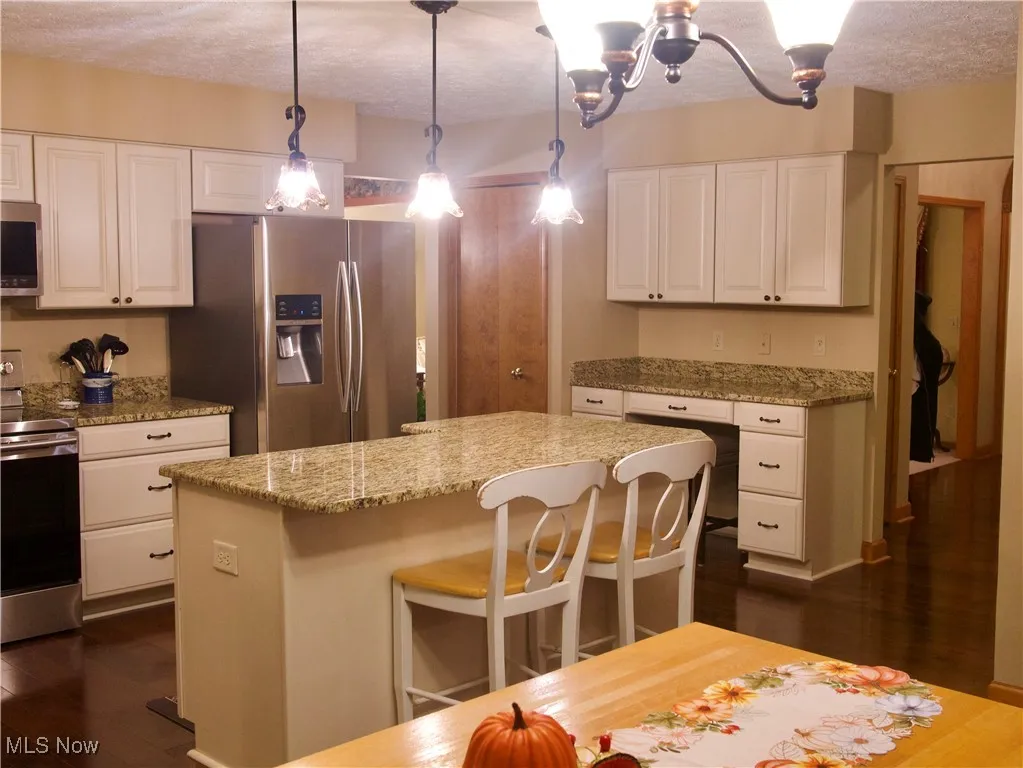 Kitchen with stainless steel appliances, a kitchen bar, dark wood finished floors, white cabinetry, and a textured ceiling