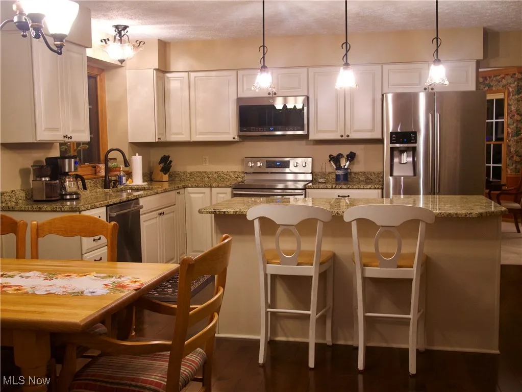 Kitchen with appliances with stainless steel finishes, hanging light fixtures, a kitchen breakfast bar, and light stone countertops