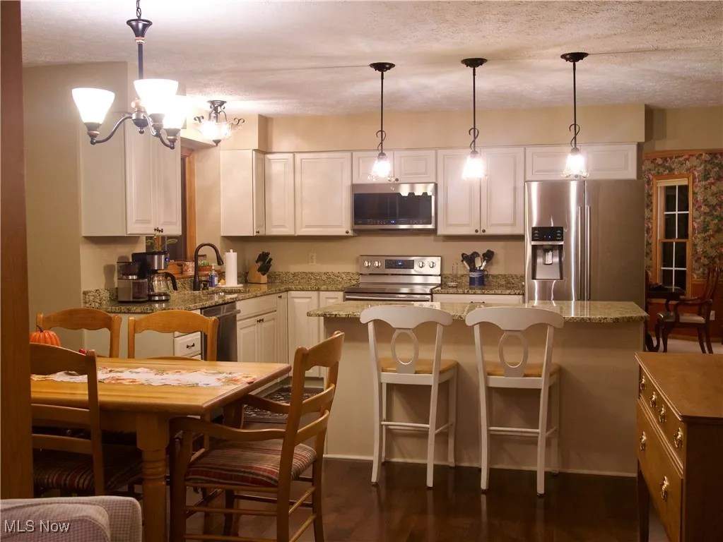 Kitchen featuring appliances with stainless steel finishes, a kitchen bar, decorative light fixtures, light stone countertops, and a textured ceiling