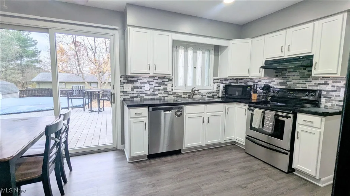 Closer view of Eat In Kitchen with Newer LVT Flooring, White Cabinets, Stainless Steel Range and Dishwasher, Sliders leading to Two Tier Deck and Fully Fenced Yard