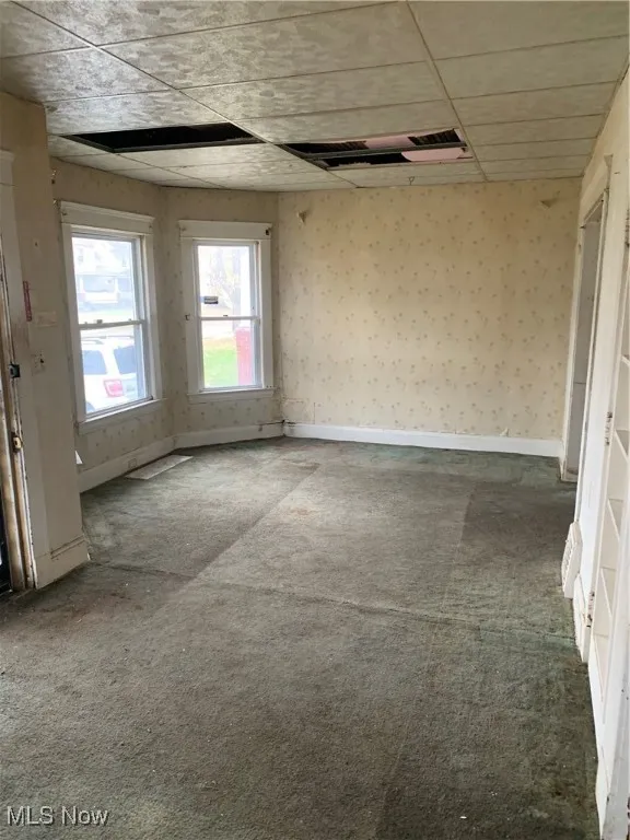 Carpeted spare room with a paneled ceiling and wallpapered walls