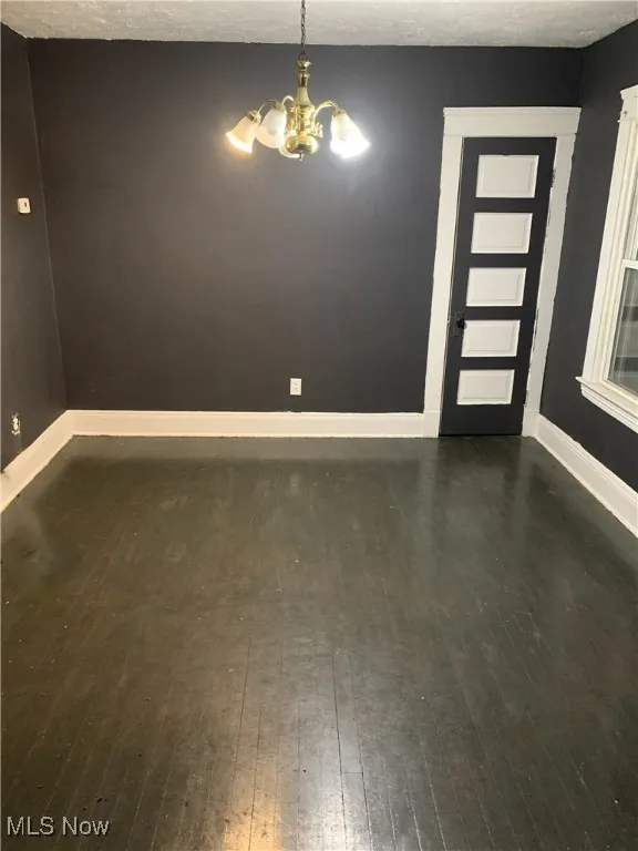 Spare room with dark wood finished floors, a chandelier, and a textured ceiling