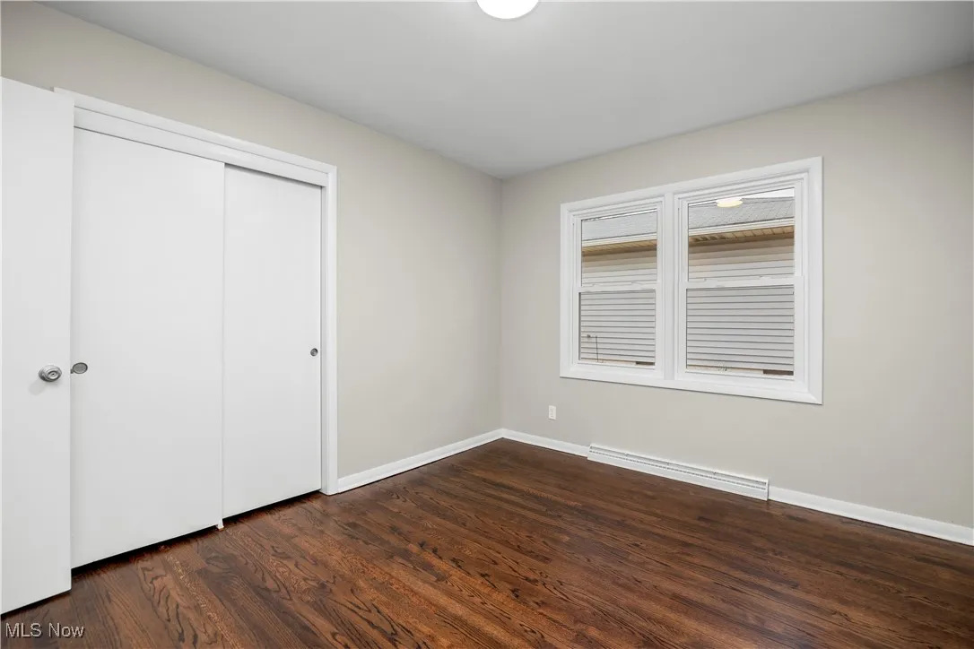 Unfurnished bedroom featuring a closet, a baseboard heating unit, and dark wood-style floors