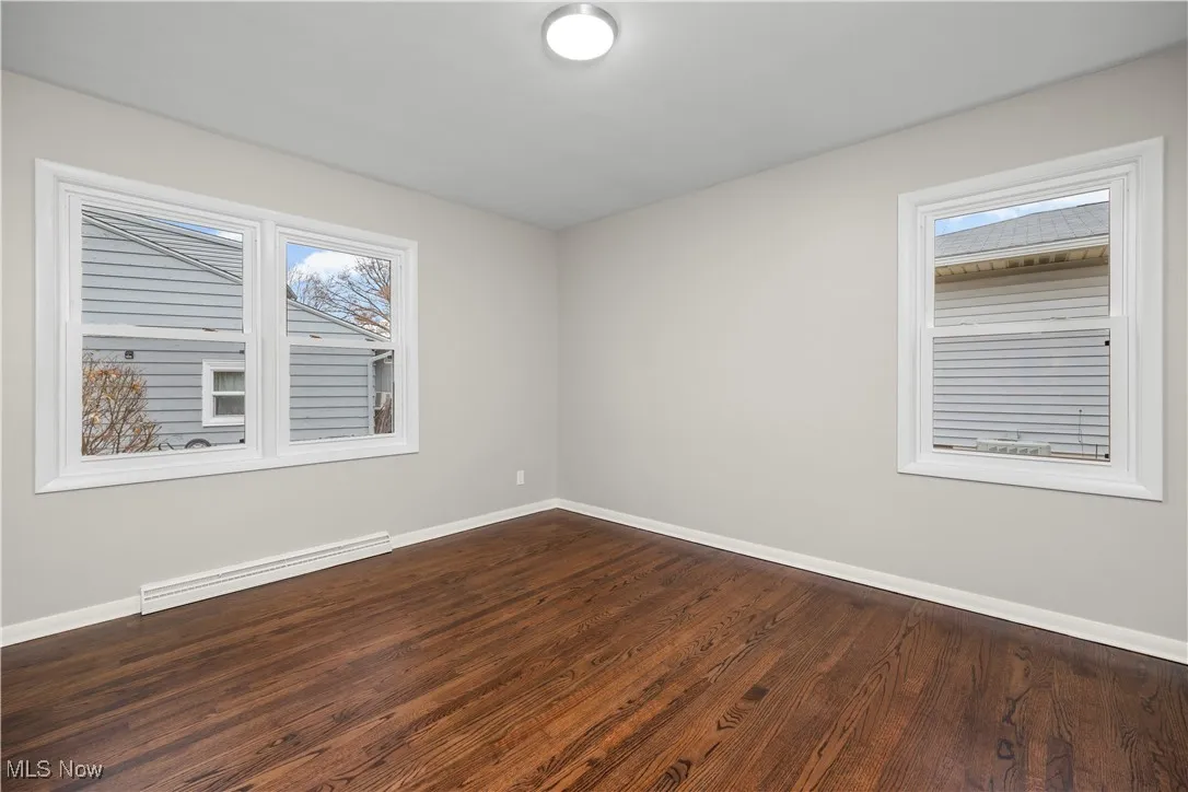 Spare room with a baseboard heating unit and dark wood-type flooring