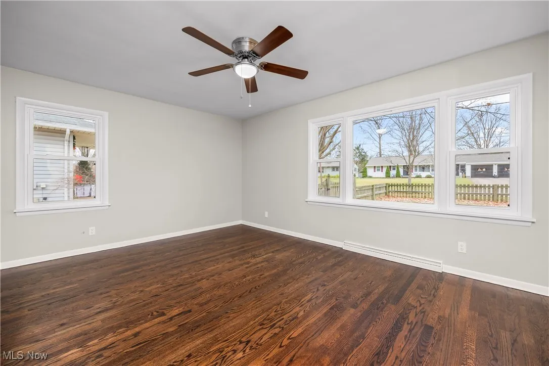 Spare room with dark wood-style flooring, a baseboard heating unit, healthy amount of natural light, and a ceiling fan