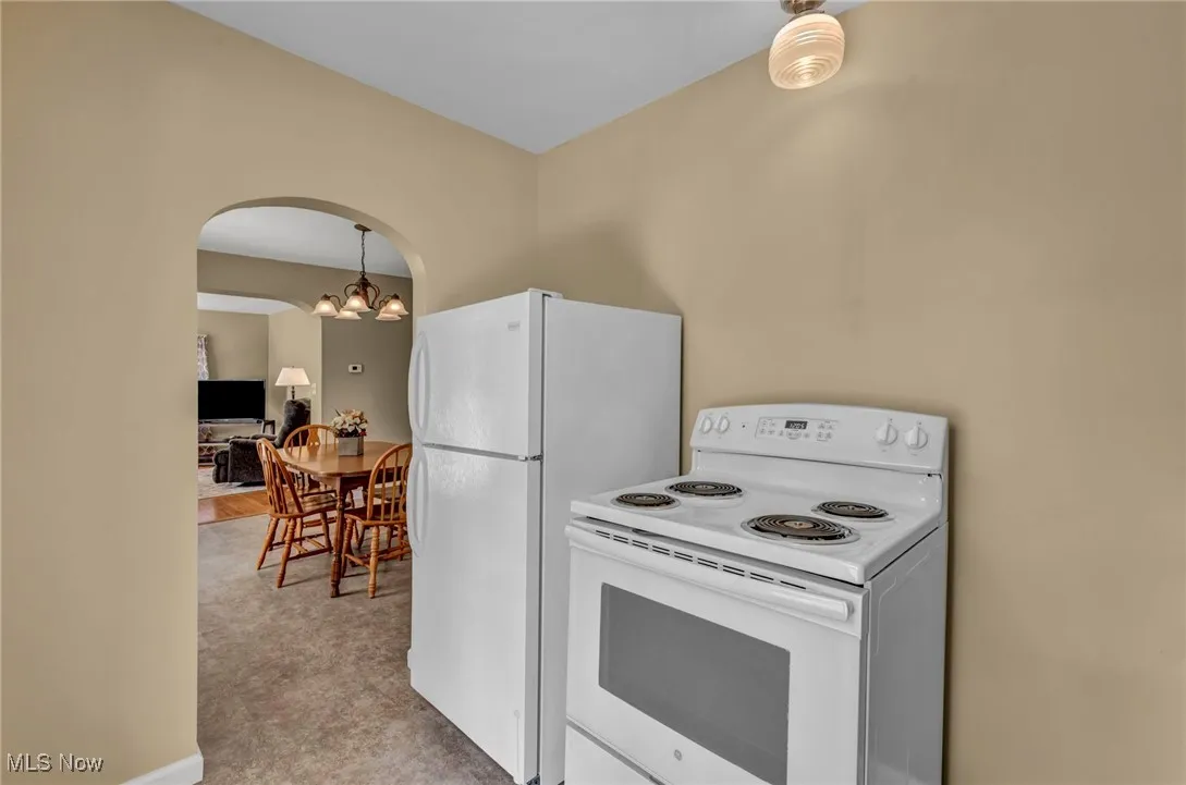 Kitchen featuring white appliances, arched walkways, a chandelier, and hanging light fixtures