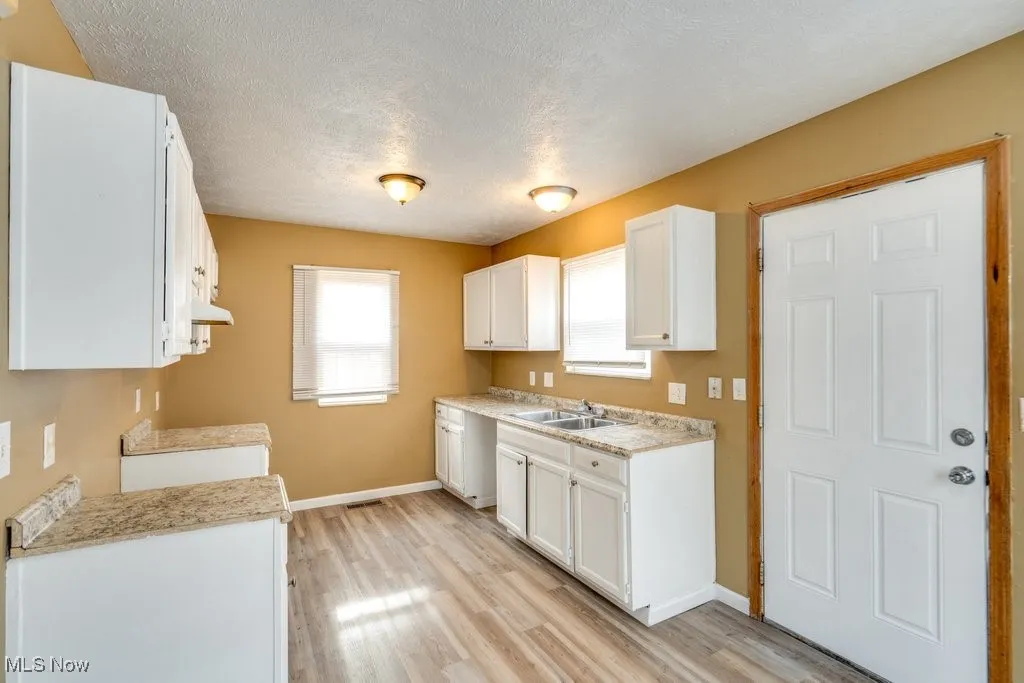 Kitchen with white cabinets, a textured ceiling, light wood-style flooring, and under cabinet range hood