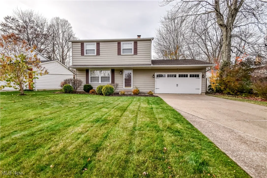 View of front facade with a garage, driveway, a front lawn, and a shingled roof