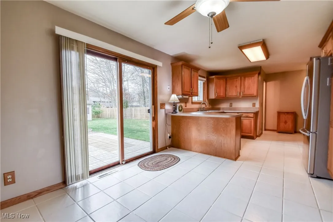 Kitchen with light countertops, freestanding refrigerator, a ceiling fan, a peninsula, and brown cabinets