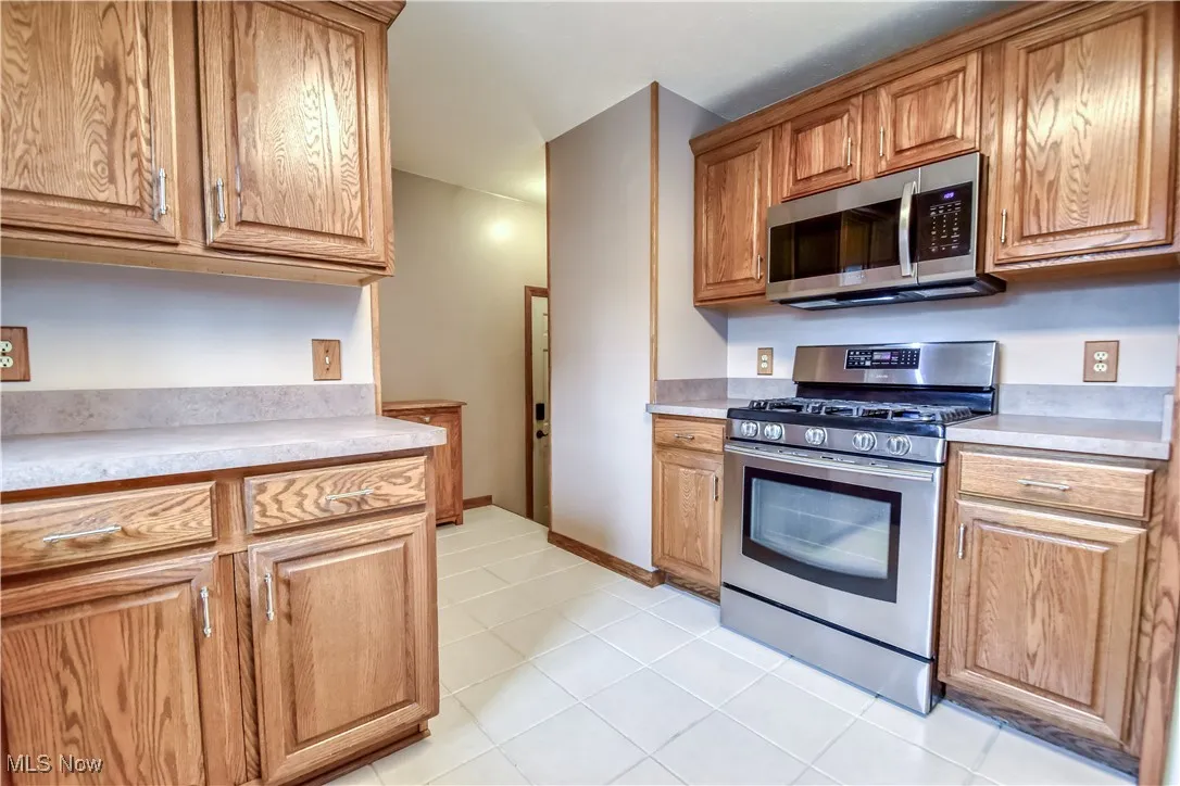 Kitchen featuring stainless steel appliances, light countertops, light tile patterned flooring, and brown cabinetry