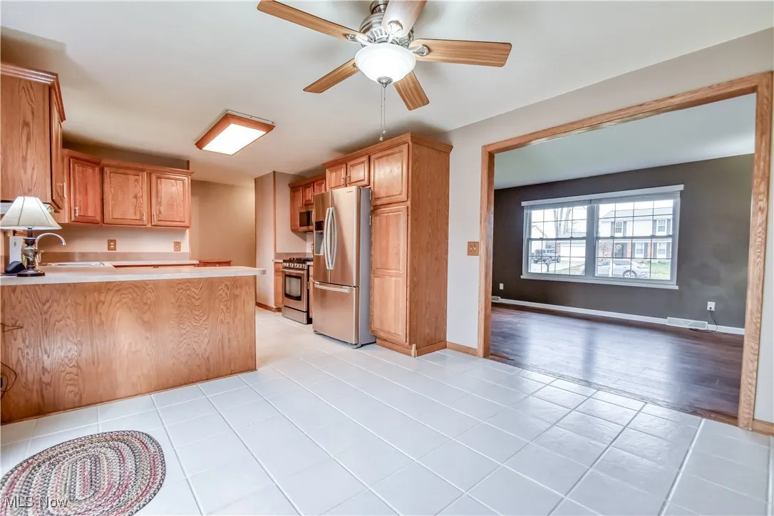 Kitchen with appliances with stainless steel finishes, light countertops, a peninsula, ceiling fan, and light tile patterned flooring