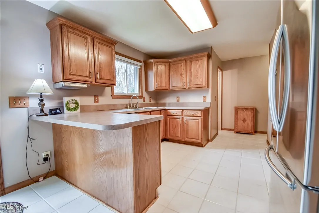Kitchen with freestanding refrigerator, a peninsula, light countertops, light tile patterned flooring, and a kitchen breakfast bar