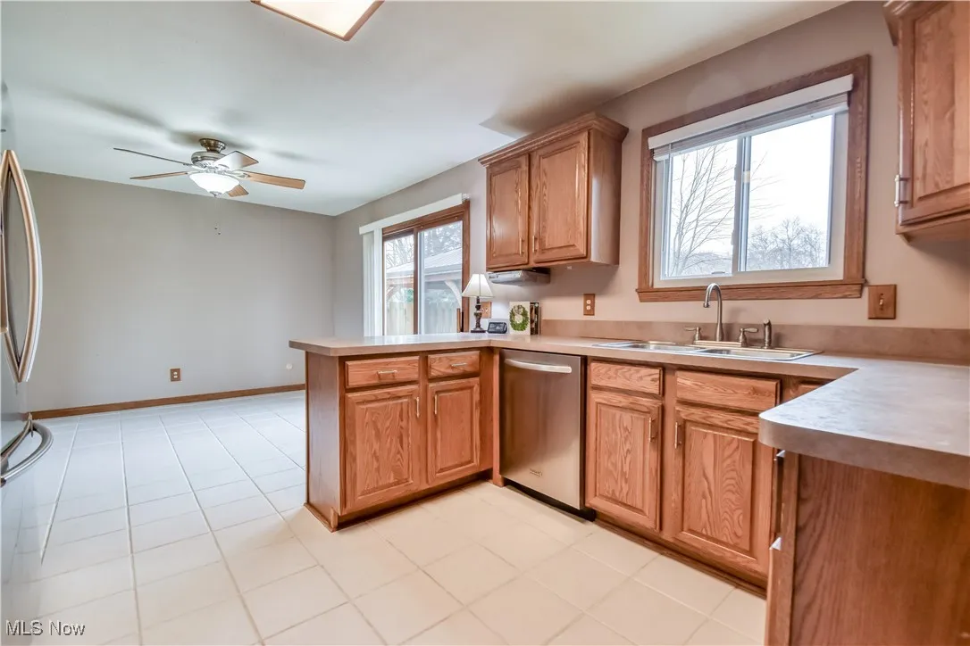 Kitchen featuring light countertops, a peninsula, stainless steel appliances, ceiling fan, and brown cabinetry