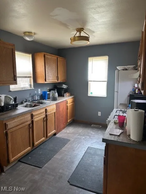 Kitchen with brown cabinets, freestanding refrigerator, dark flooring, dark countertops, and a textured ceiling
