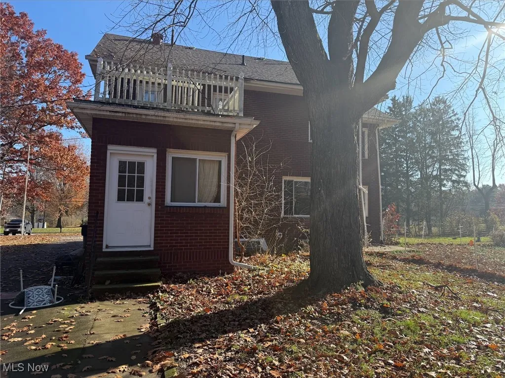 Rear view of house featuring brick siding, entry steps, and a balcony