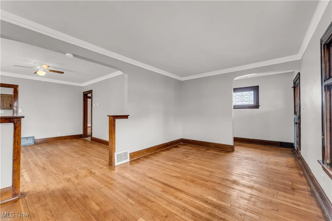 Unfurnished room featuring arched walkways, light wood finished floors, crown molding, and ceiling fan