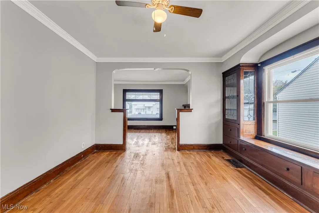 Spare room featuring crown molding, light wood-type flooring, arched walkways, and ceiling fan