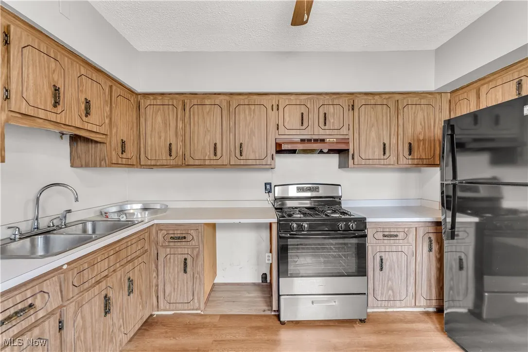 Kitchen featuring stainless steel gas range oven, light countertops, light wood finished floors, a textured ceiling, and freestanding refrigerator