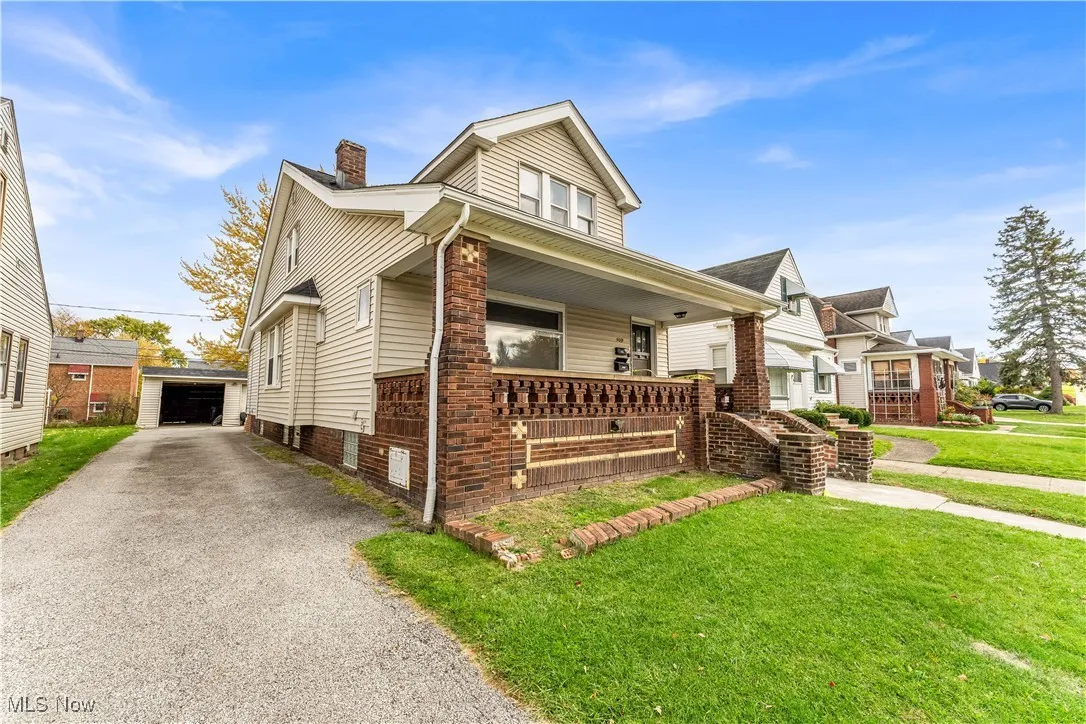 Bungalow-style house featuring a porch, a front yard, an outbuilding, a detached garage, and a chimney