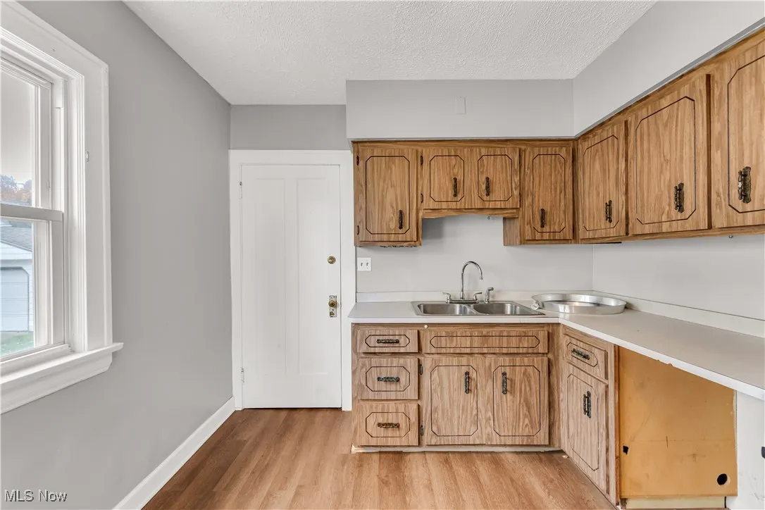 Kitchen with light countertops, healthy amount of natural light, brown cabinetry, light wood finished floors, and a textured ceiling